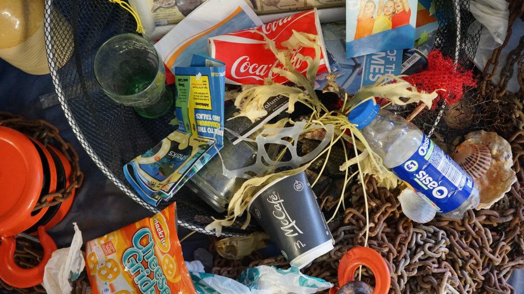 Trash, including plastic bottles, metals chains, and glassware, found in the ocean.