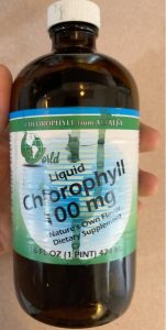 An amber bottle held by a hand. The label, with blue and green accents, reads: Liquid Chlorophyll, 100 mg. 