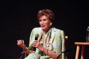 Photograph of Dr. Edith Eger sitting in a chair, talking into a microphone at a TEDxSanDiego event