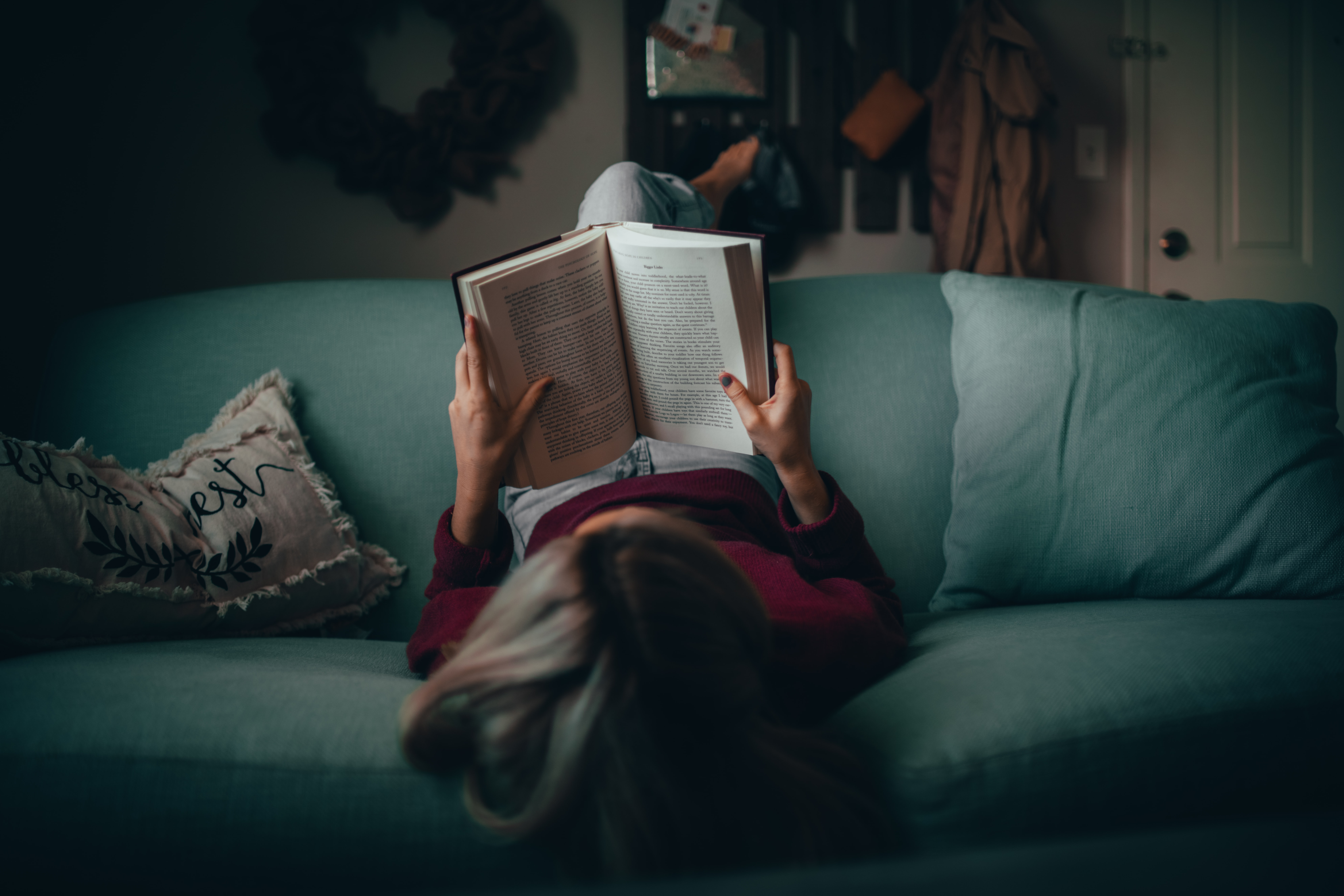 Photo of a woman sitting upside down on a couch reading a book