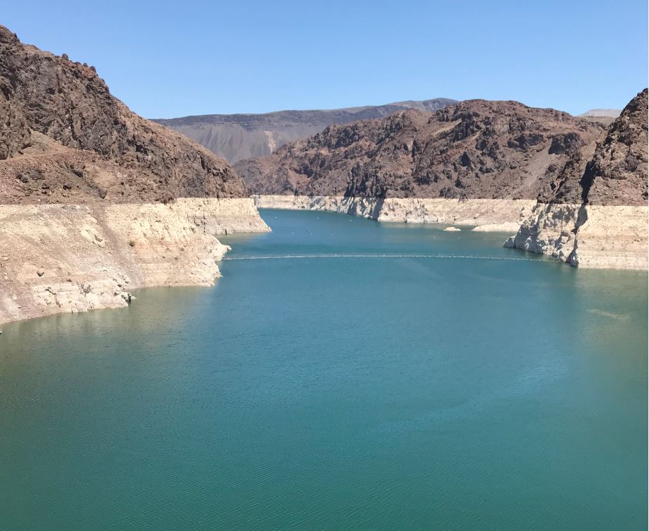 Photograph of Lake Mead reservoir, a large body of blue water surrounded by two-tone rocky mountainous walls that show the previous waterline. 