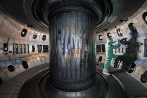 An image of a reaction chamber of a nuclear fusion reactor. The interior of the chamber is the size of a small bedroom with walls coated in metal. There is a central pillar also coated in metal. The design showcases the enviroment needed to create fusion in a Tokamak reactor. 