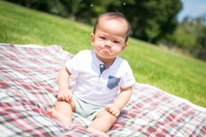 Baby with upset face sitting on a picnic blanket