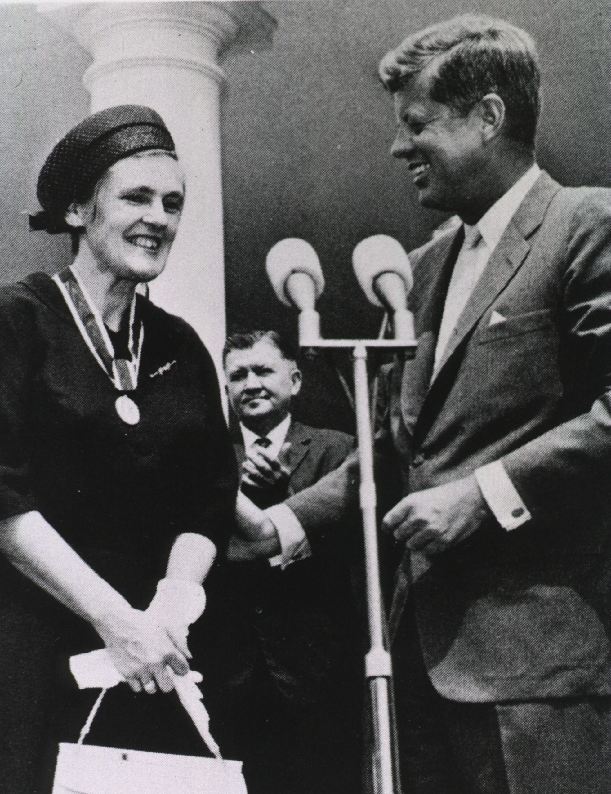 Frances Oldham Kelsey at a microphone with President John F. Kennedy receiving a medal.